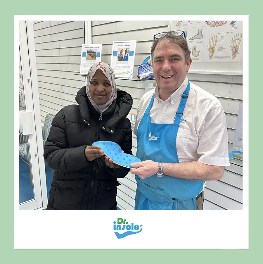 Customer at the Dr Insole clinic holding a blue custom orthotic insole after receiving support for leg length discrepancy which caused foot and back pain, assisted by a staff member.