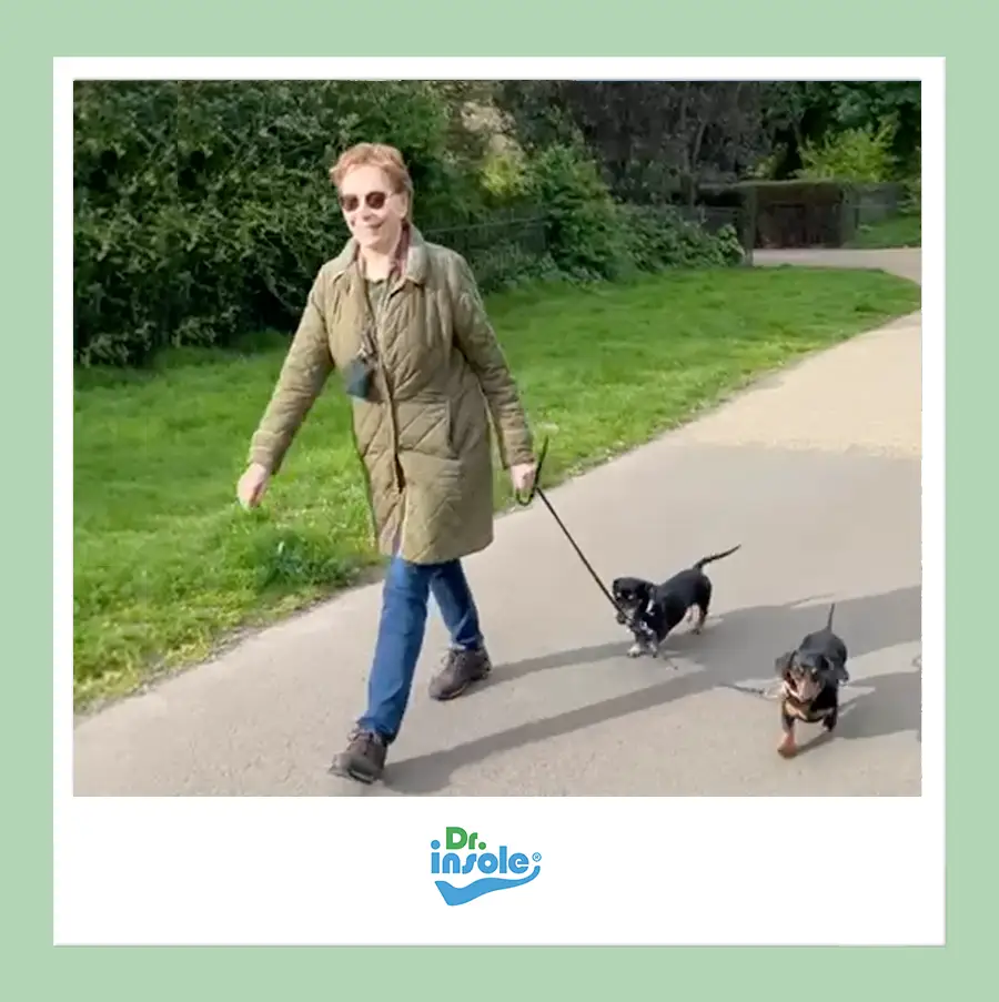 Customer walking comfortably outdoors with Dr Insole orthotics, shown while walking two small dogs in the park.