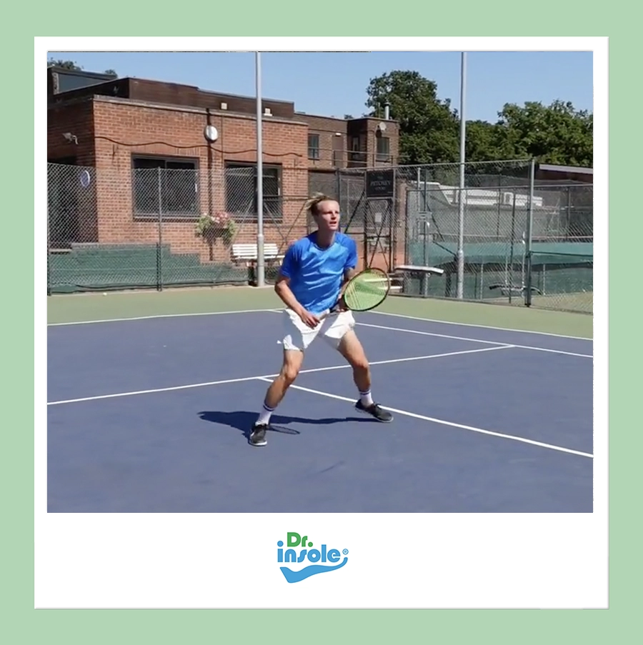 Competitive tennis player on an outdoor court preparing for a shot while wearing custom orthotic insoles from Dr. Insole.